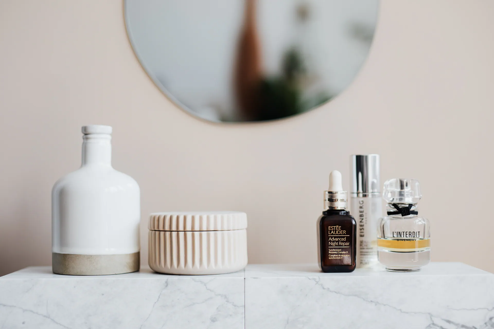 Bottles, a ribbed jar and perfume on a marble shelf, shown as a style reference